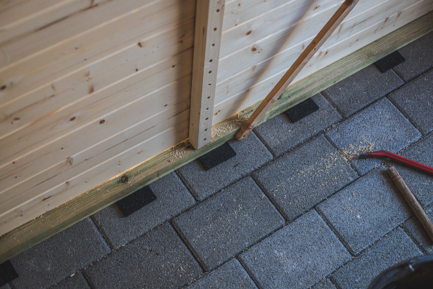 Nachdem das Gartenhaus an seine endgültige Position gesetzt wurde, werden Pads aus Gummigranulat untergelegt.