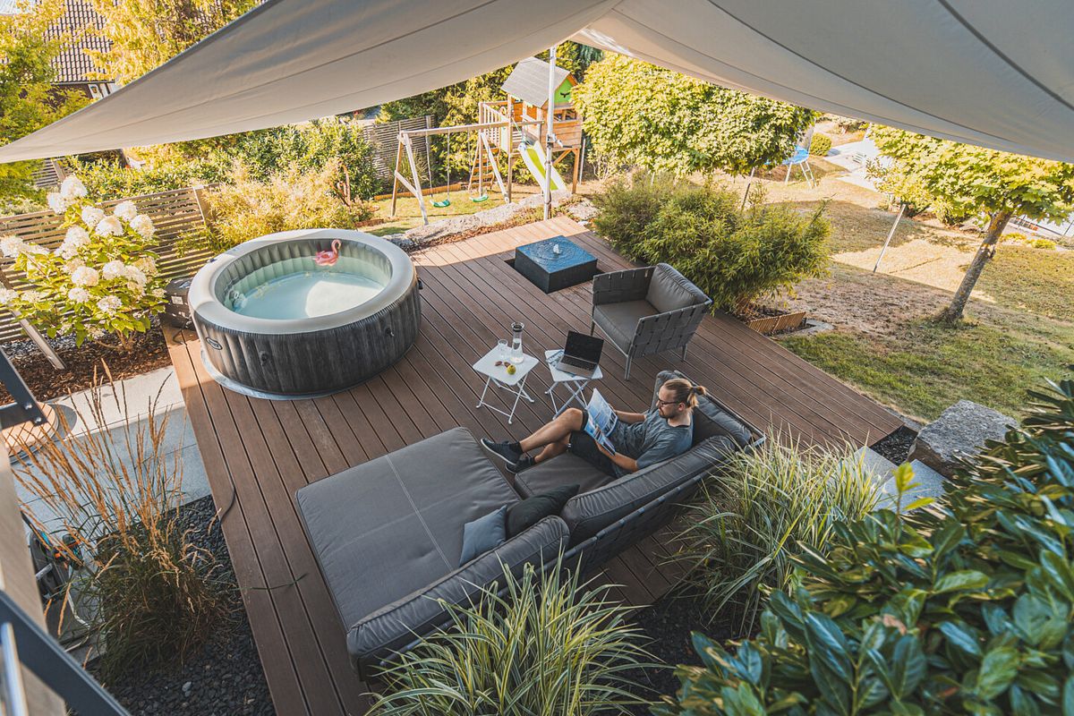 Eine gemütliche Terrasse im Grünen mit Sofa und Terrassenstühlen neben einem schönen Gartenteich